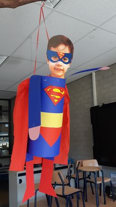 a boy in a superman costume hanging from a ceiling with chairs and tables behind him