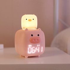 a pink pig alarm clock sitting on top of a white table next to a bed