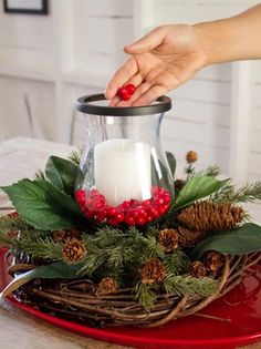 a candle is lit on top of a red tray with greenery and pine cones