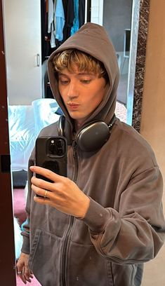 a young man wearing headphones looking at his cell phone while standing in front of a mirror