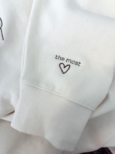 two white shirts with embroidered words on the front and back, one has a heart