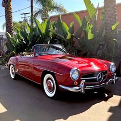 an old red convertible car parked in front of a building with palm trees behind it