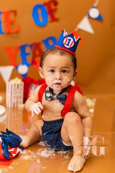 a baby boy sitting on the floor wearing a red, white and blue birthday hat