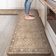 a woman standing on top of a rug in a kitchen next to an oven and cabinets