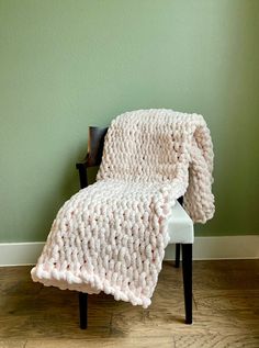 a white chair sitting in front of a green wall with a knitted blanket on it