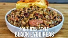 a bowl filled with black eyed peas next to a piece of bread on top of a wooden table