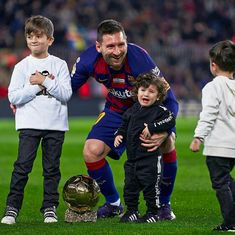 a man kneeling on top of a soccer ball next to two small boys and an adult