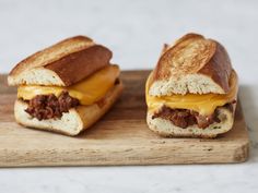 two sandwiches with cheese and meat are sitting on a cutting board