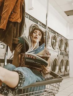 a woman reading a book while sitting in a laundry machine with her legs up on the floor