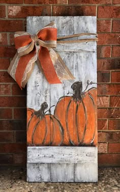 a wooden sign with pumpkins painted on it and a bow hanging from the front