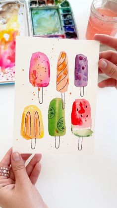 a person holding up a card with watercolors on it and ice cream pops