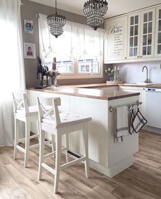 a kitchen with white cabinets and counter tops next to two chairs in front of an island