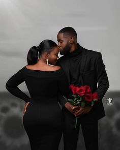 a man and woman standing next to each other in front of a dark background with red roses