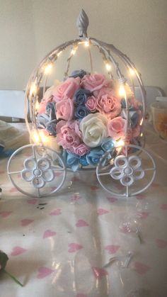 a flower arrangement in a glass carriage with fairy lights on the sides and pink roses inside