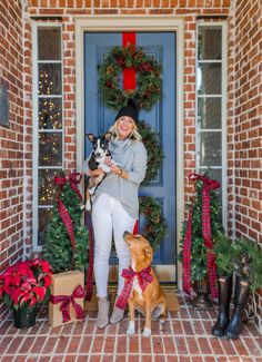 a woman standing in front of a blue door with two dogs and presents on the doorstep