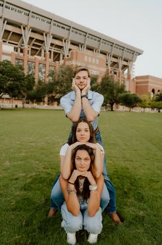 three people sitting on the grass in front of a building with an empty field behind them