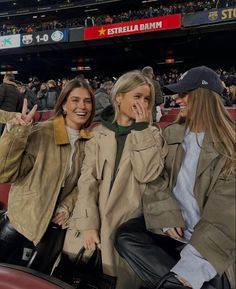 two women sitting next to each other in the stands at a baseball game with their hands up