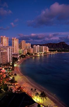 an aerial view of the beach and city lights at night, with mountains in the background