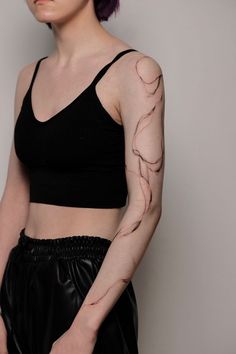 a woman with purple hair and tattoos on her arm is posing for the camera in front of a white wall