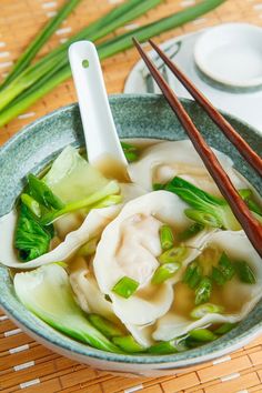 a bowl filled with dumplings and vegetables next to chopsticks on a table