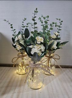 three glass vases with flowers and lights in them