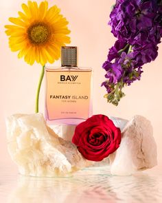 two flowers are next to a bottle of bay fantasy island perfume on a pink background