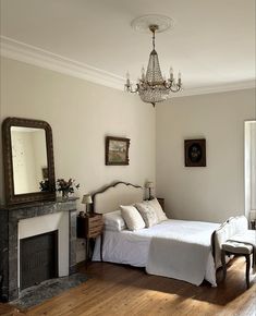 a bedroom with a bed, fireplace and chandelier hanging from the ceiling in front of a mirror