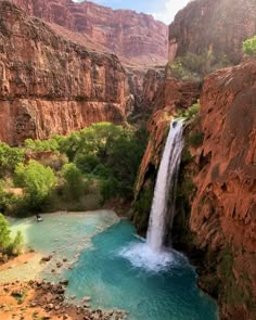 a waterfall in the middle of a canyon with blue water and green trees around it