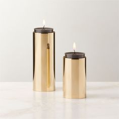 two gold candle holders sitting on top of a white counter next to each other,