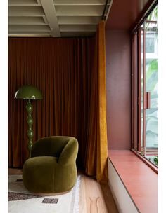 a green chair sitting in front of a window next to a lamp on top of a wooden floor