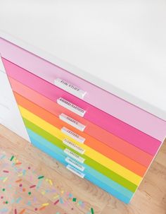 a multicolored file cabinet sitting on top of a wooden floor next to a white wall