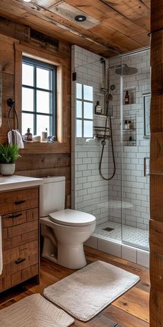 a white toilet sitting next to a shower in a bathroom under a window on top of a wooden floor