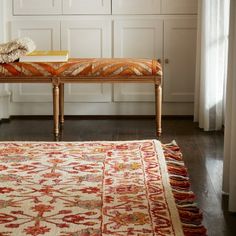 a bench sitting in the middle of a living room next to a rug on top of a hard wood floor