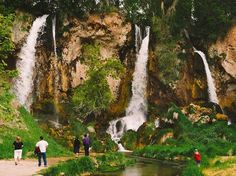 several people are standing in front of a waterfall with water cascading over it