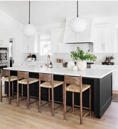 a kitchen with white cabinets, black island and wooden stools in front of an oven