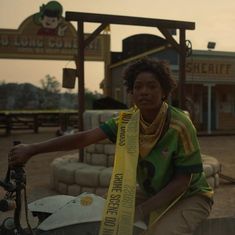 a woman sitting on top of a motorcycle with a yellow ribbon around her neck and wearing a green shirt