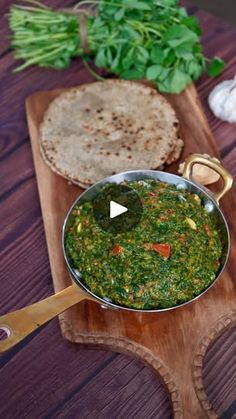 a wooden cutting board topped with a metal pan filled with green vegetables and pita bread