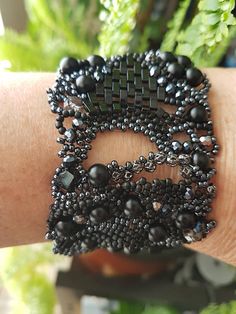 a woman's arm with black beaded bracelets on it and a potted plant in the background