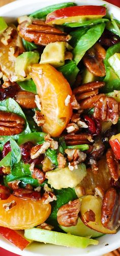 a salad with oranges, apples, and pecans is shown in a bowl