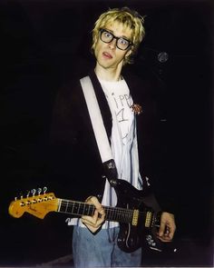 a young man with glasses playing an electric guitar