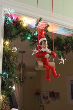 an elf is hanging from the ceiling in front of a mirror with christmas lights on it