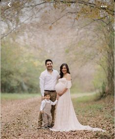 a pregnant couple and their son pose for a family photo in the woods with leaves on the ground