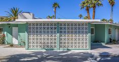 a house with palm trees in the background and a blue sky behind it that has a large, geometric design on the front door