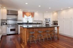 a large kitchen with white cabinets and stainless steel appliances, along with hardwood flooring