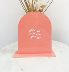 there is a small pink vase with flowers in it on the table next to a white wall