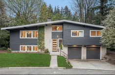 a large gray house with lots of windows and trees in the back ground, surrounded by green grass