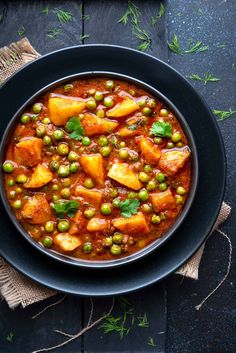 a black bowl filled with peas and potatoes on top of a wooden table next to a napkin