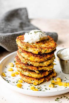 a stack of corn fritters on a white plate with a small bowl of sour cream