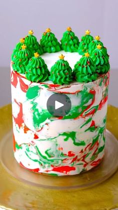 a decorated cake with green frosting and trees on top, sitting on a gold platter