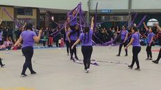 a group of people standing on top of a basketball court holding up purple ribbons in the air